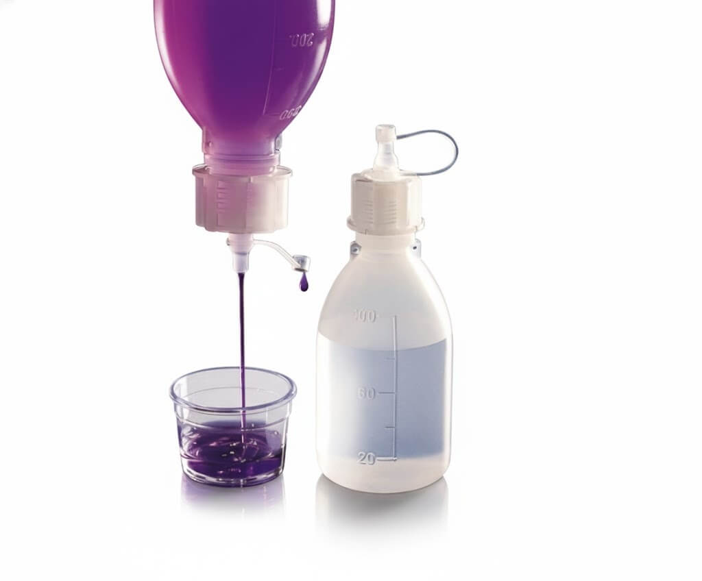 Transparante kunststof doseerfles met schroefdop en korte tuit, gebruikt voor nauwkeurige dosering van vloeistoffen. Links wordt een vloeistof overgebracht in een glas.